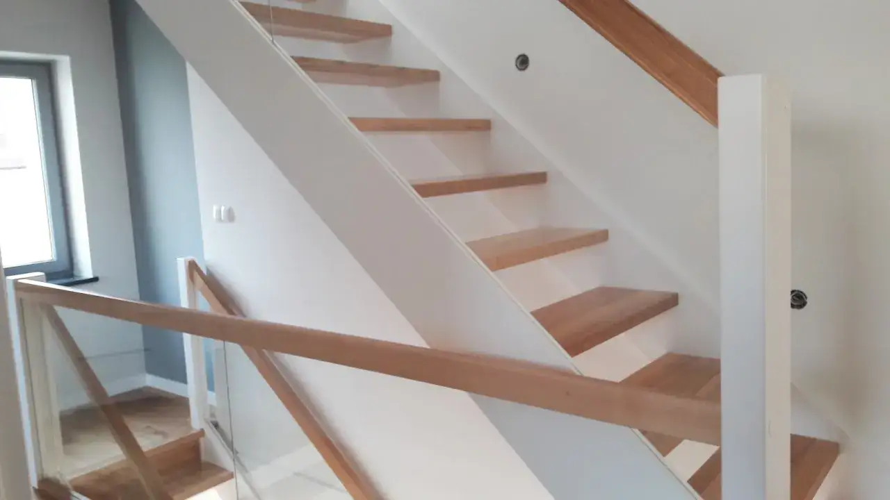 Nowoczesne schody policzkowe z drewnianymi stopniami i szklaną balustradą.