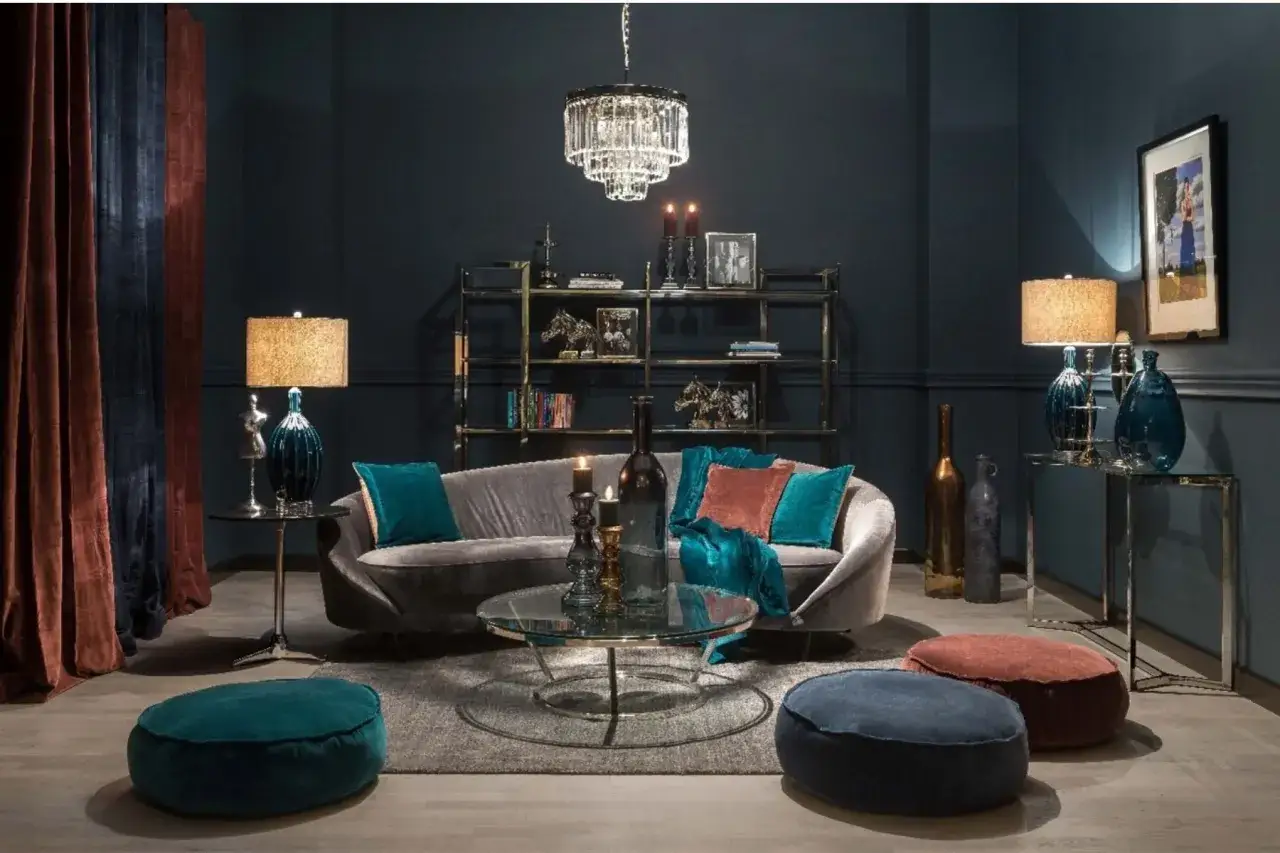 Elegancki salon z sofą w odcieniu grafitu, turkusowymi i rudymi poduszkami. W tle regał, a na nim ozdoby. Dominujący kolor navy ścian i zasłon tworzy przytulną atmosferę.