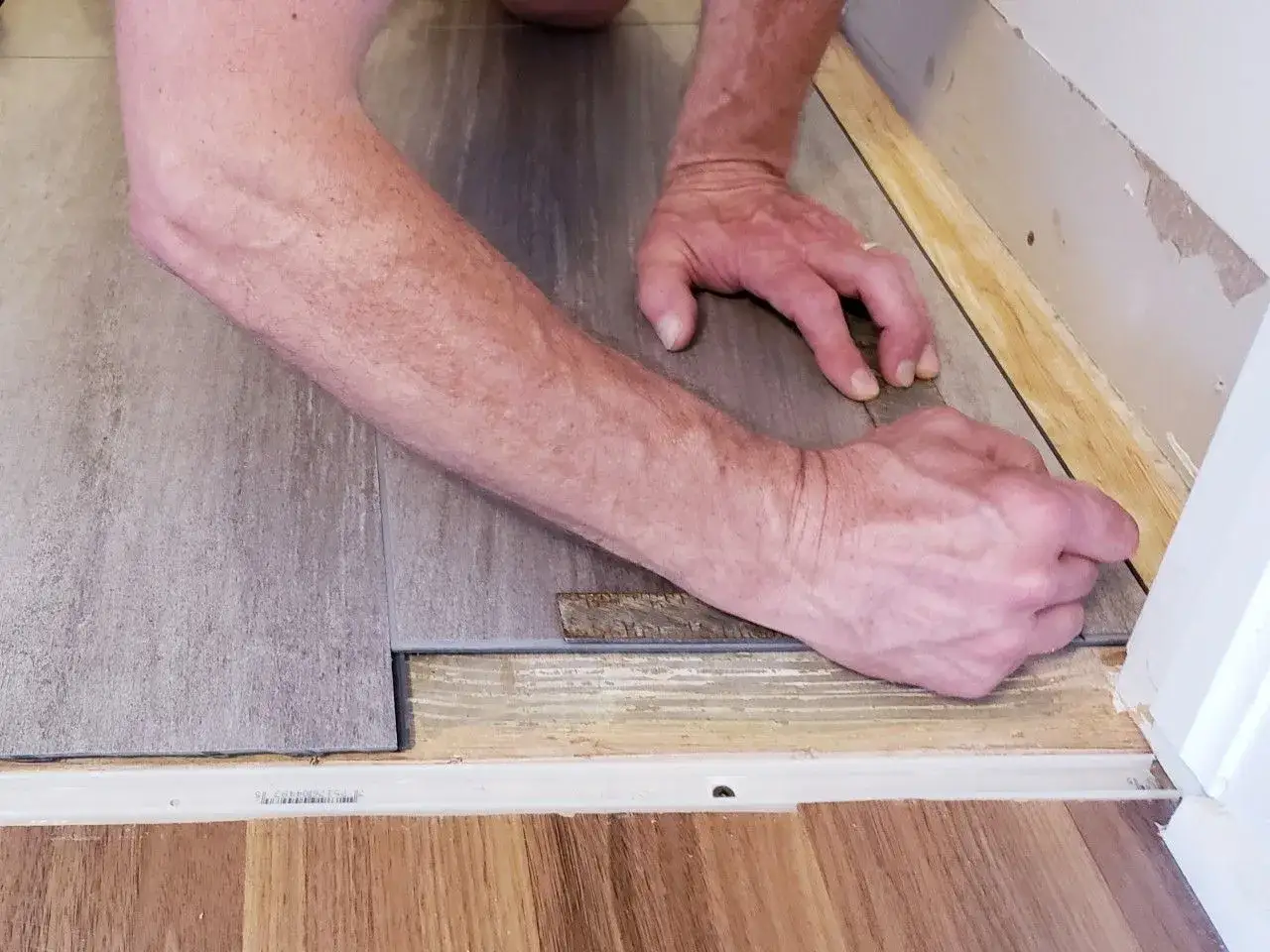Ręce układają szarą płytkę winylową, tworząc płynne łączenie płytek z panelami podłogowymi.