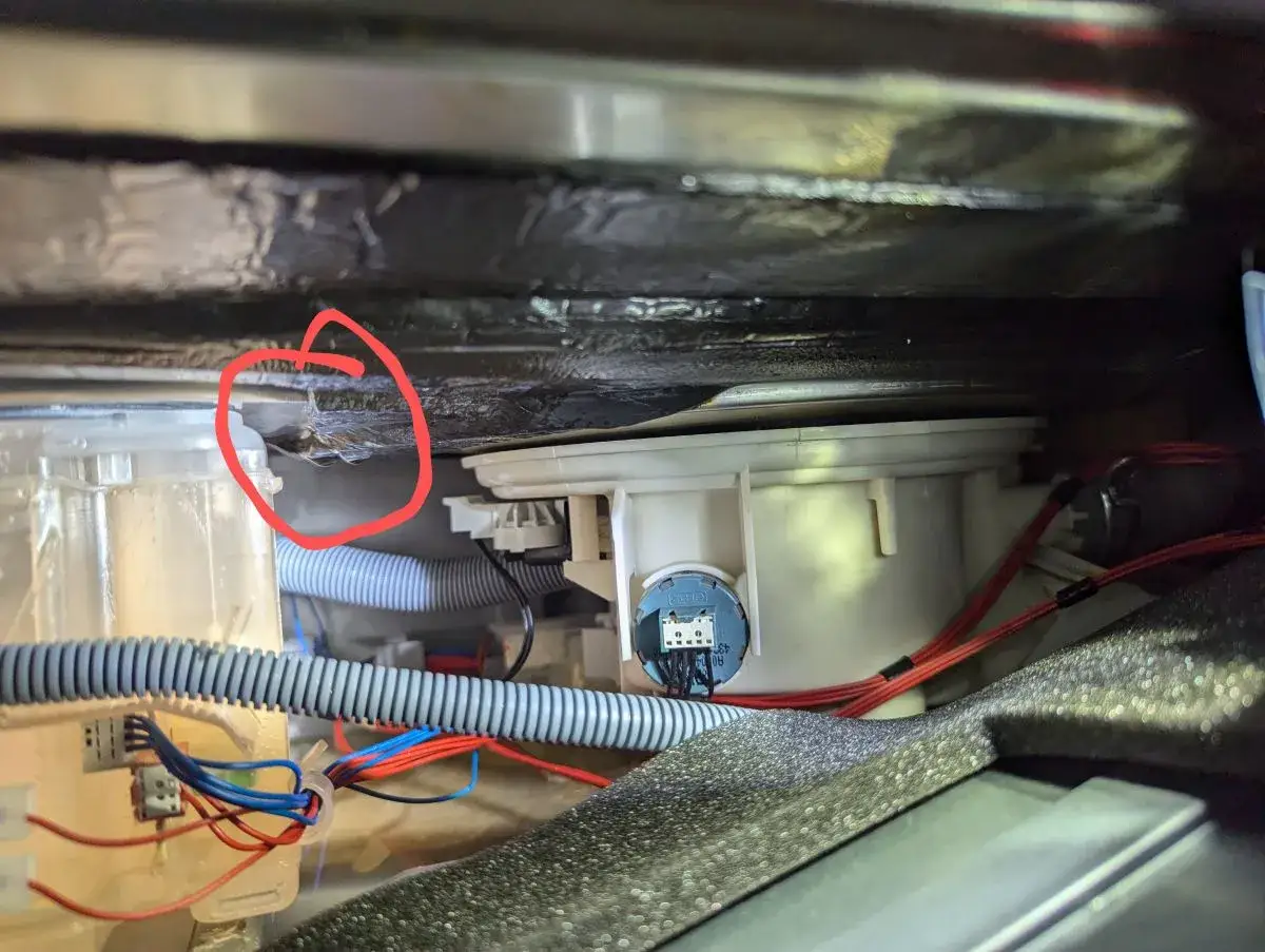 Wyciek wody pod zmywarką Electrolux, prawdopodobnie przyczyna błędu i30. Widać mokrą izolację i elementy pompy.