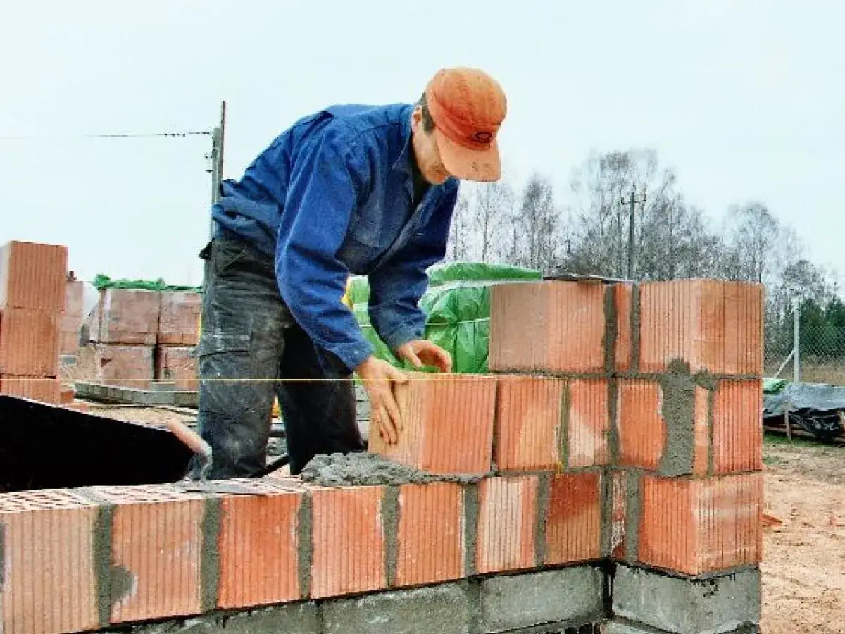 Murarz układa pustaki, używając piana do murowania. Budowa domu postępuje.